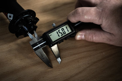 Mechanic using Unior 270A digital caliper to measure a mountain bike hub axle at 15.01 mm on a workshop bench