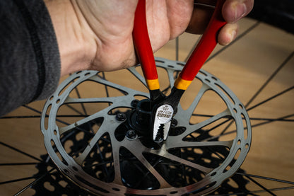 Mechanic using red Unior 407/4P screw grabbing pliers to remove a stripped center-lock bolt from a bicycle disc brake rotor