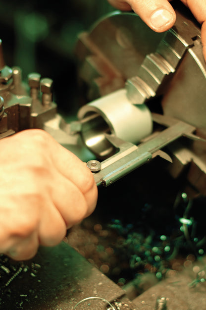 Machinist measuring a small turned part with Unior vernier caliper at a lathe chuck on the factory floor