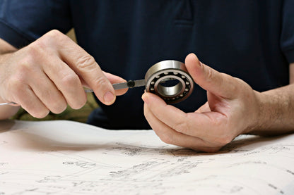 Mechanic measuring a sealed bicycle hub bearing with Unior vernier caliper, engineering drawings on the workbench