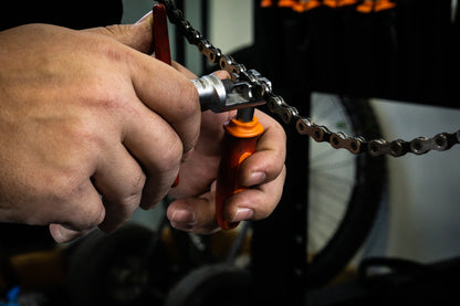 Mechanic using Unior Professional Chain Tool to break a worn bicycle chain on the workstand, T-bar engaged