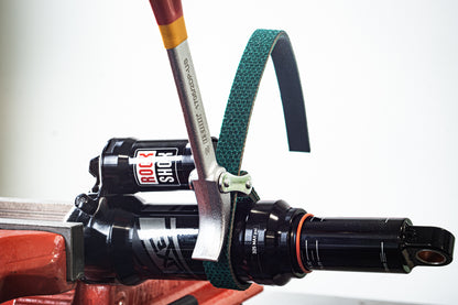 Unior strap wrench in use on a RockShox rear shock clamped in a workshop vise, green strap wrapped around the air can