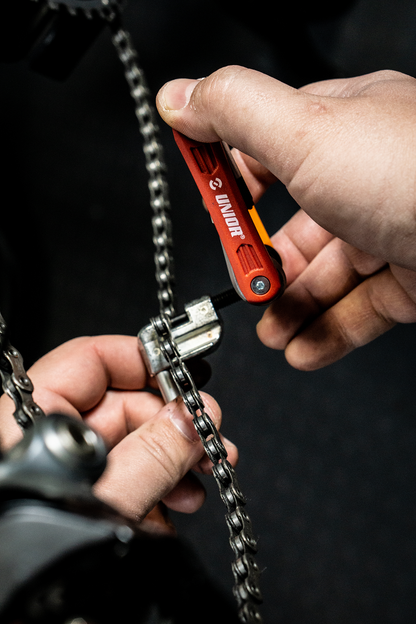 Mechanic using Unior Multitool EURO6 on a bicycle chain at the workstand, drivetrain in focus
