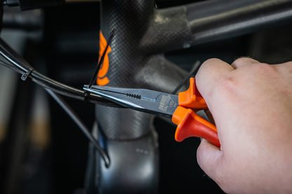 Mechanic routing internal brake hose on a carbon bicycle frame using Unior VDE-insulated long needle nose pliers