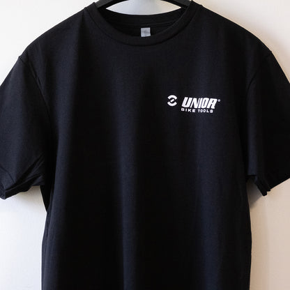 Made For Work tee shirt front close-up, white Unior Bike Tools chest logo on black cotton hanging on a wall
