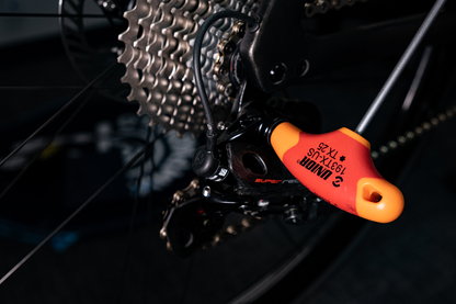 Unior T-handle ball-end hex driver adjusting a rear derailleur, bicycle cassette and chain in the background