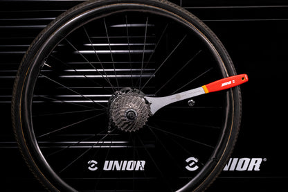 Unior Multispeed Chainwhip 1660/2DP-US resting against rear wheel cassette on a workshop wall with Unior branding