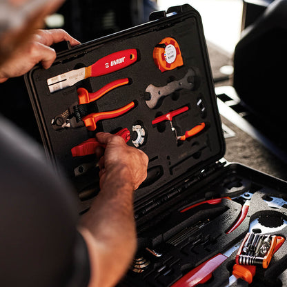 Mechanic lifting pliers from the Unior Home Kit case in a workshop, tools seated in fitted foam inside the lid