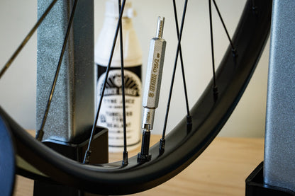 Unior Valve Core Tool 1755/2 in use at a tubeless rim valve, sealant bottle and wheel on truing stand behind