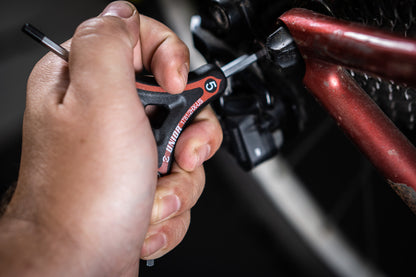 Unior 1781/2HX Three-Way Hex Y-wrench in use on a red mountain bike frame, mechanic's hand turning the contoured handle