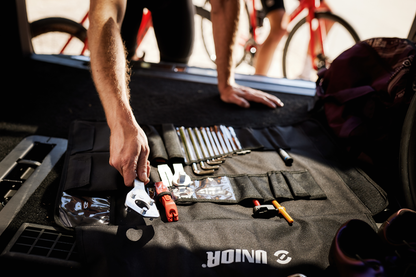 Mechanic's hand reaching into open Unior tool wrap on workshop ground beside red road bicycle at race truck